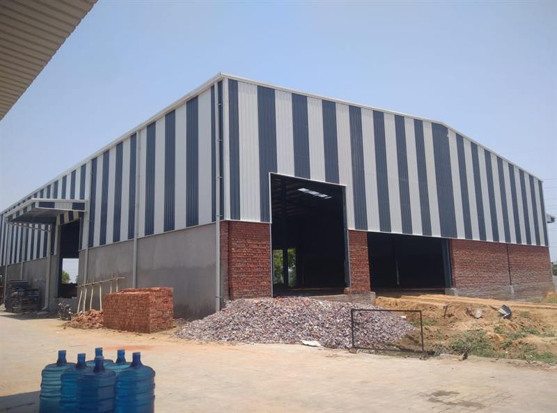 Grey and white clad pre-engineered shed with brick and aggregate stacked on site