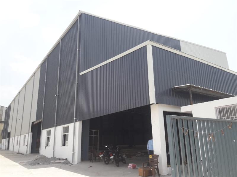 Corner elevation of a large grey pre-engineered warehouse with gated entry