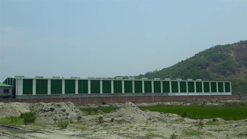 Green-clad long-span shed with hills behind